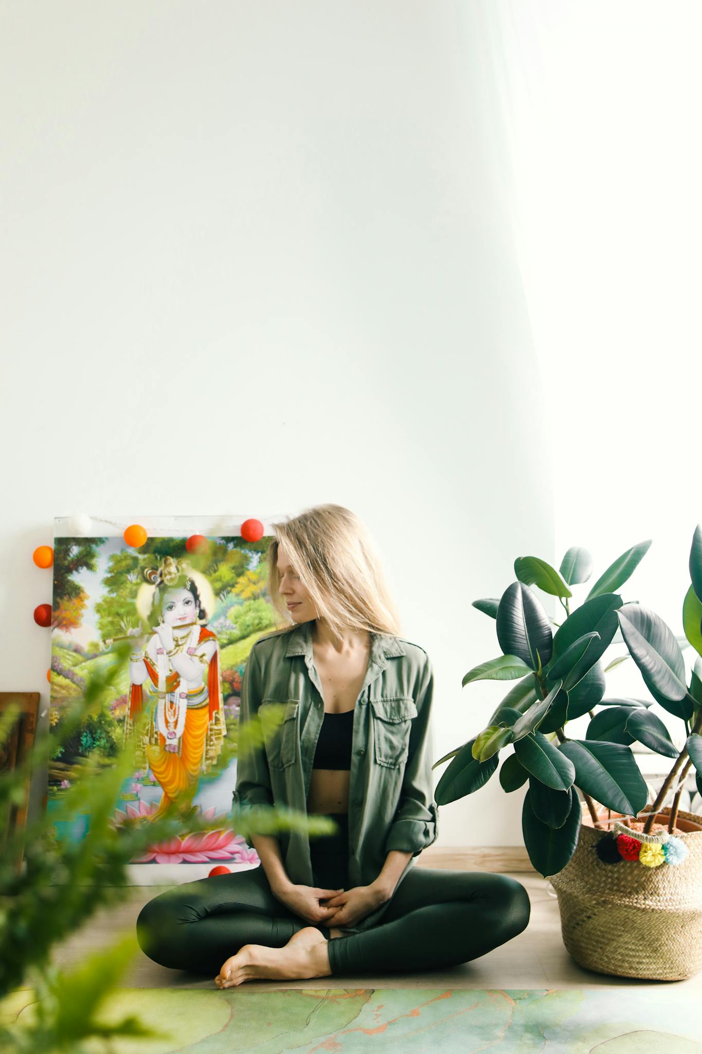 Woman practicing meditation surrounded by plants and vibrant artwork for wellness.